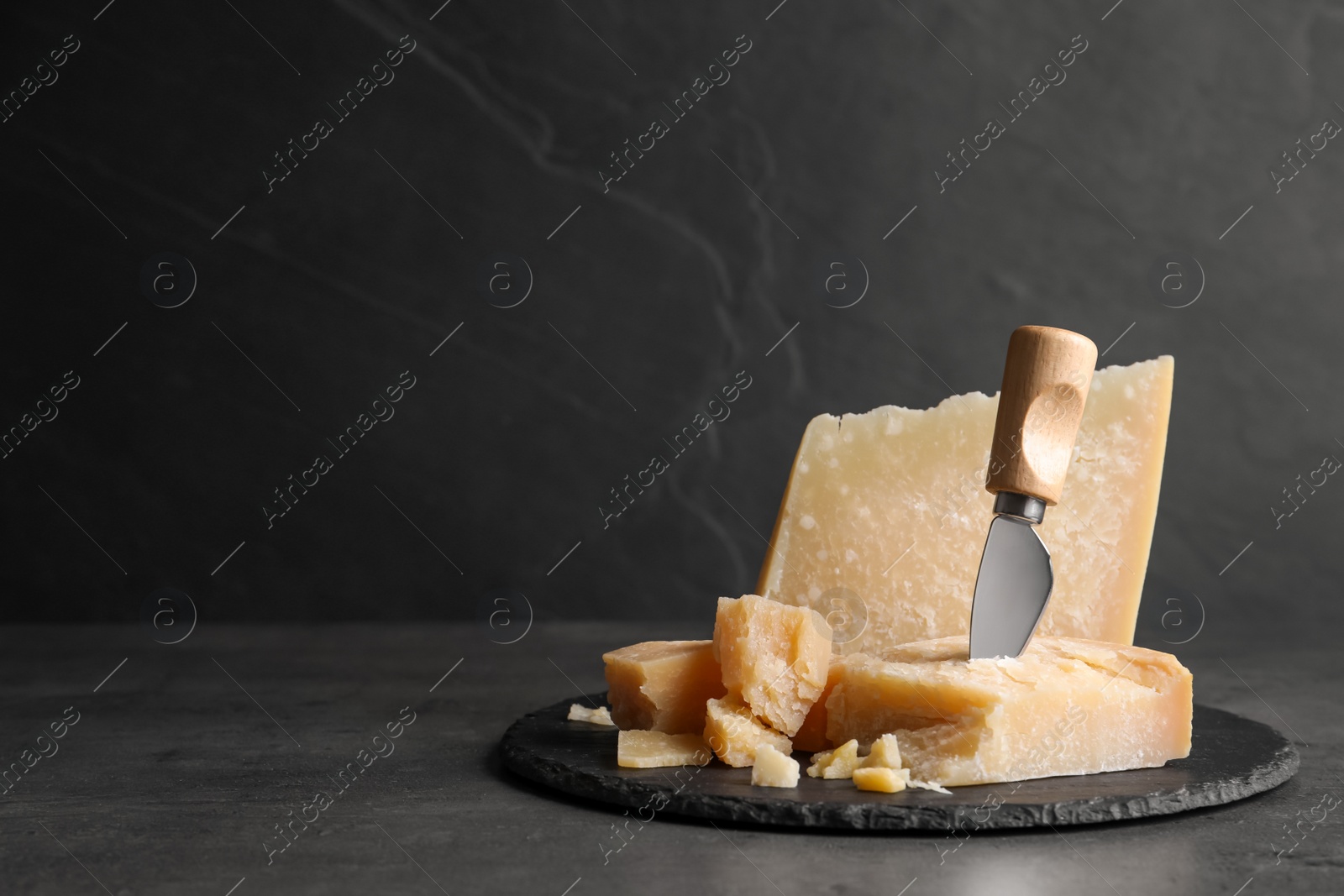 Photo of Parmesan cheese with knife on grey table. Space for text