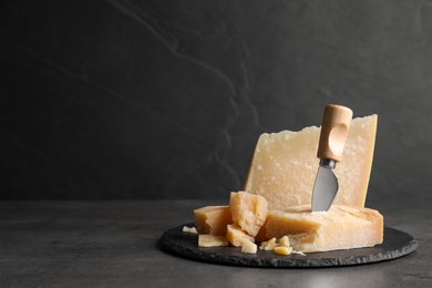 Photo of Parmesan cheese with knife on grey table. Space for text