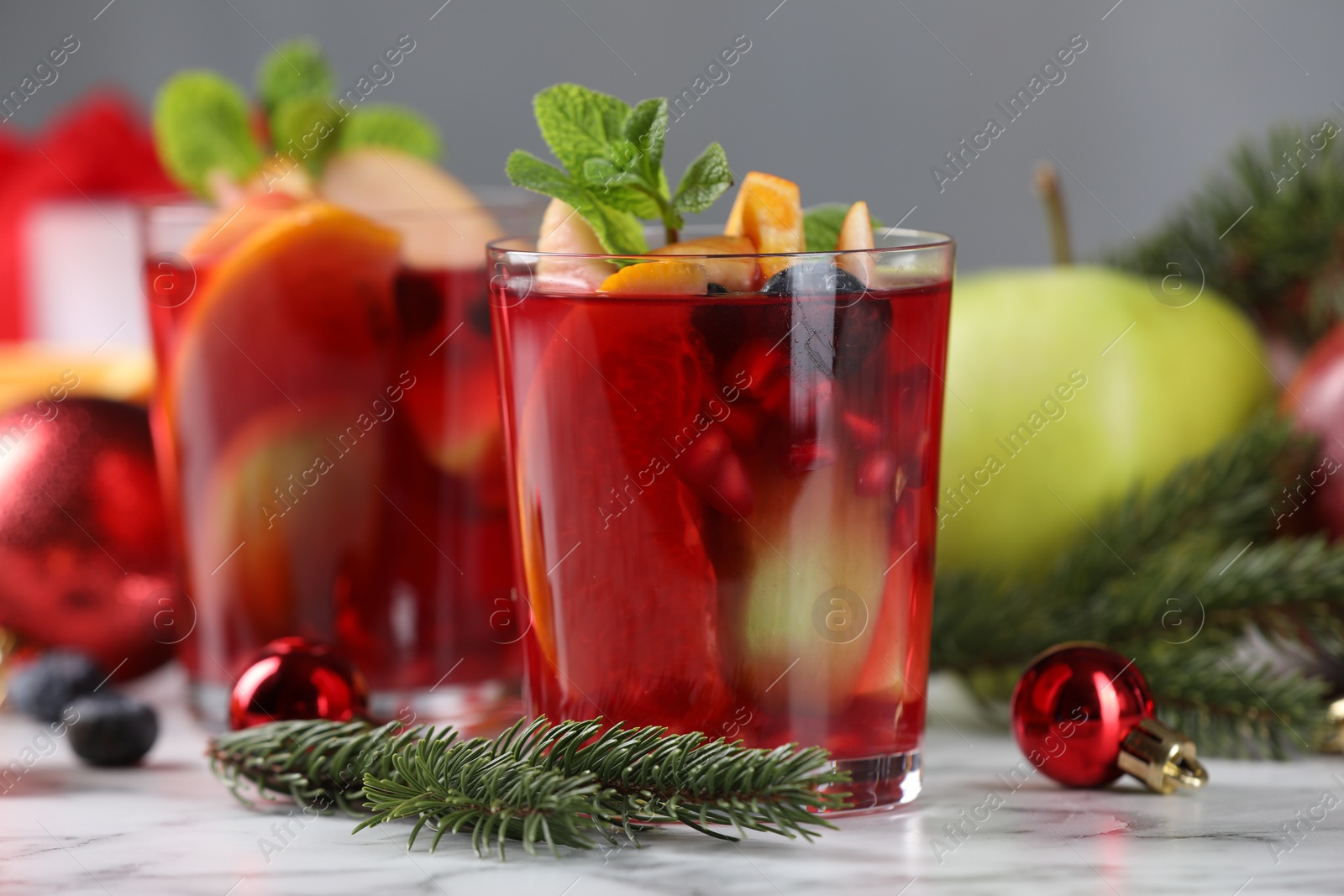 Photo of Aromatic Sangria drink in glasses, ingredients and Christmas decor on white marble table