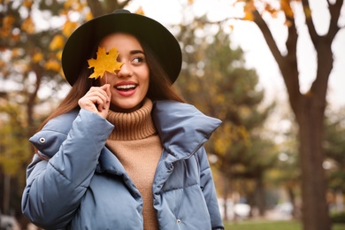 Photo of Young woman in stylish clothes holding yellow leaf outdoors, space for text. Autumn look