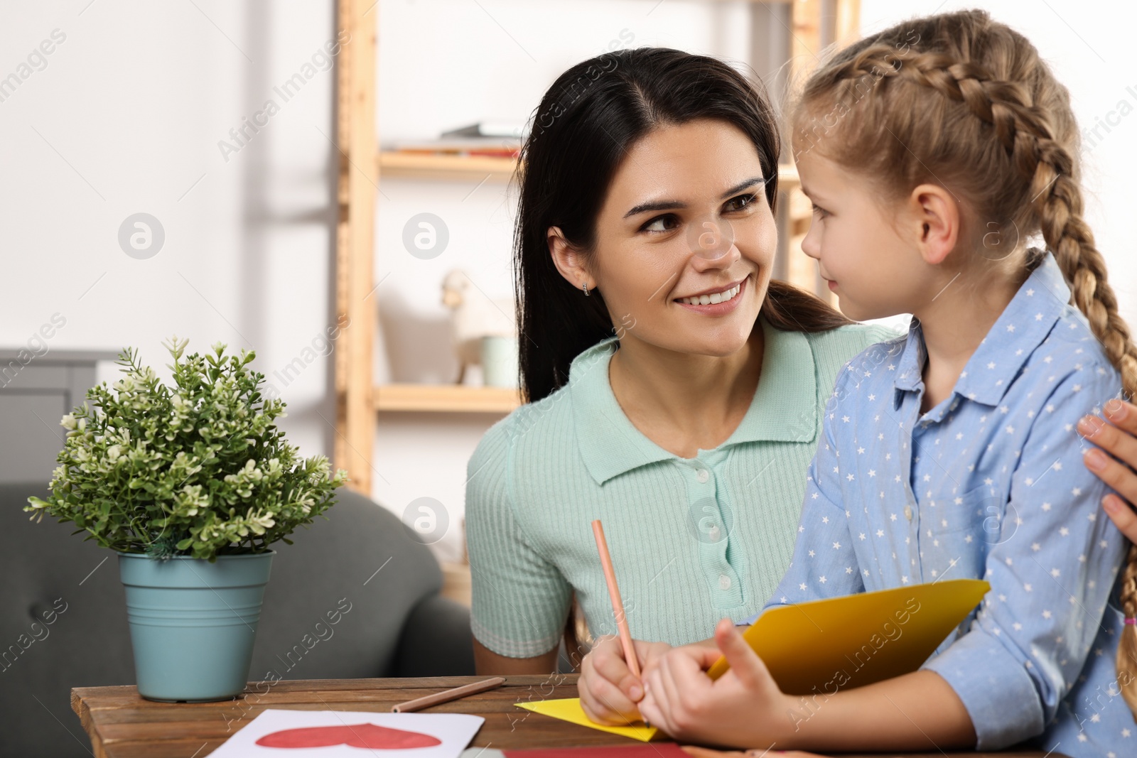 Photo of Cute little girl with her mother making beautiful greeting card at home