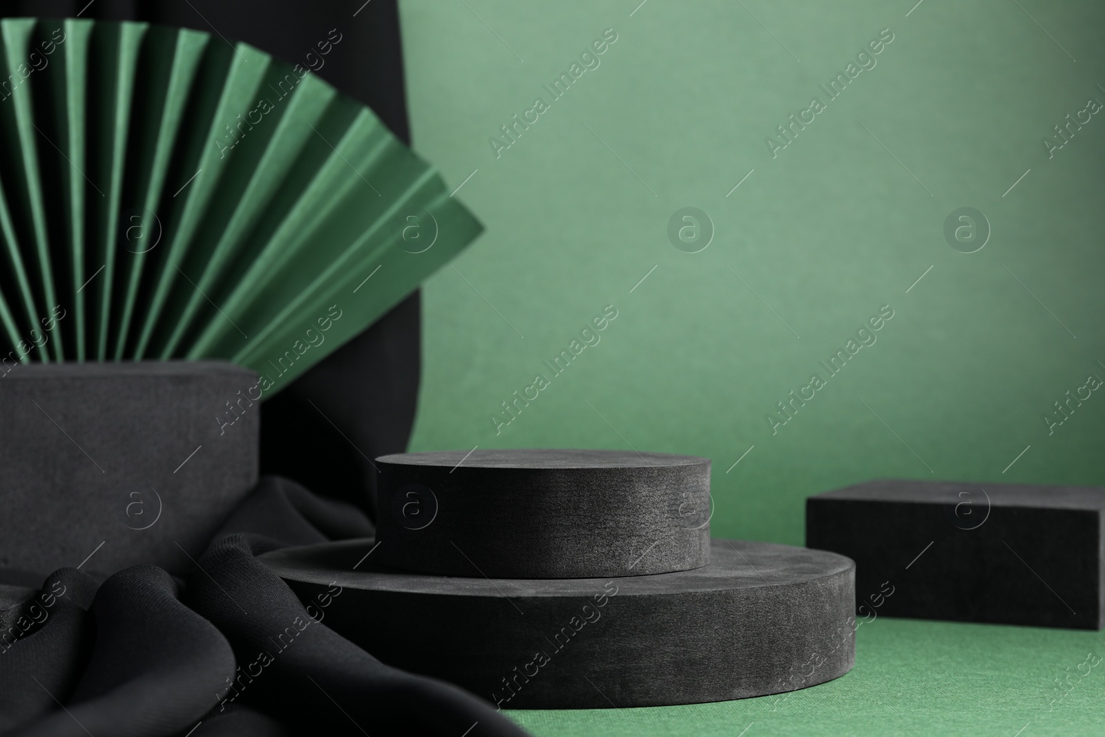 Photo of Black geometric figures and paper fan on green background. Stylish presentation for product