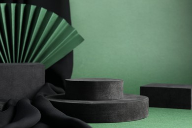 Black geometric figures and paper fan on green background. Stylish presentation for product