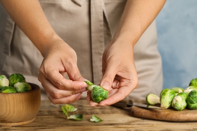 Woman peeling Brussels sprout at wooden table, closeup