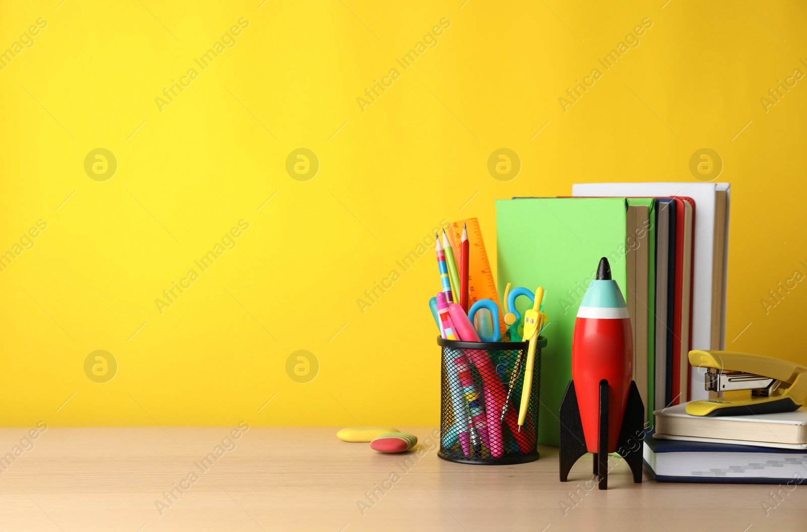 Photo of Bright toy rocket and school supplies on wooden table. Space for text