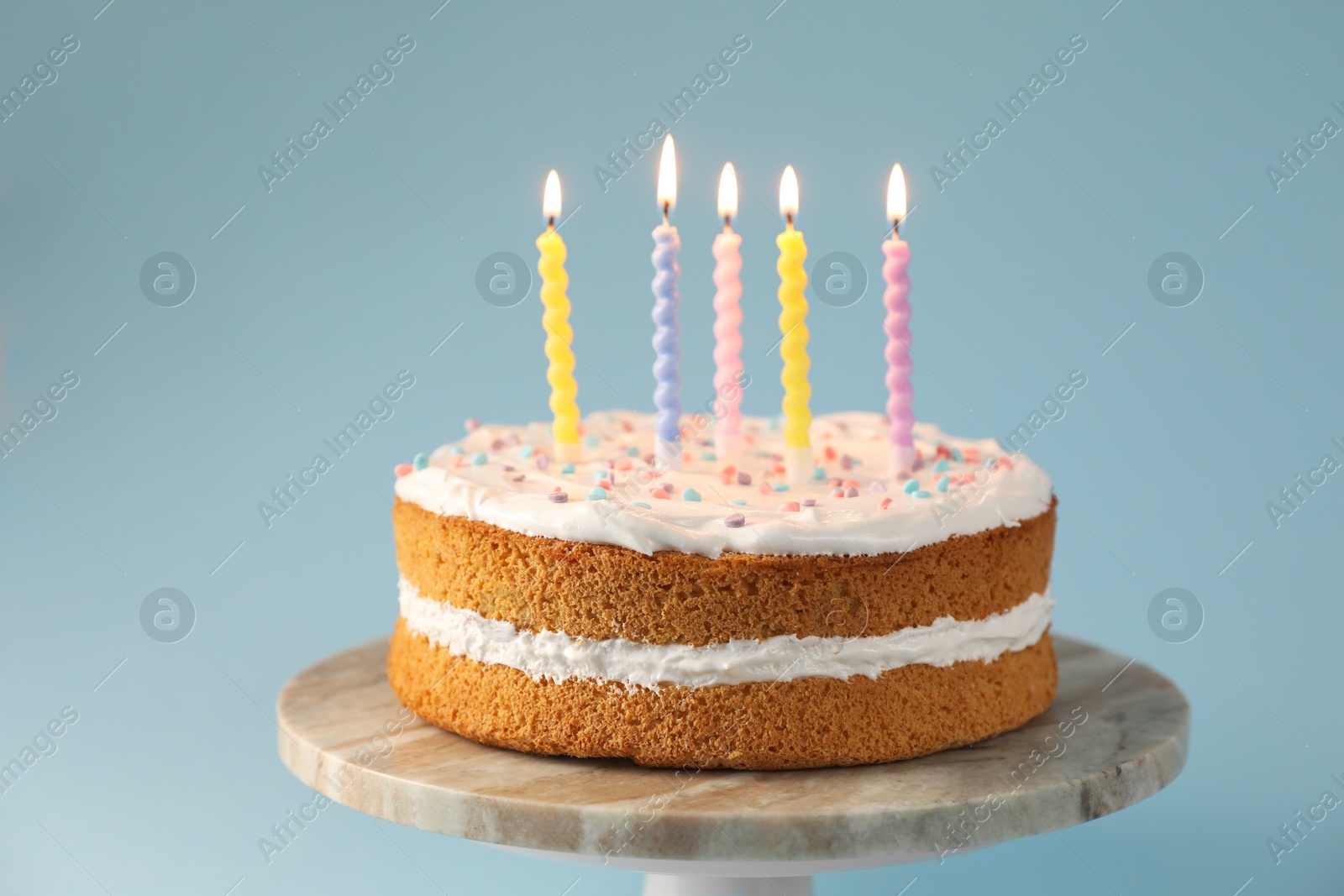 Photo of Tasty cake with colorful candles on light blue background, closeup