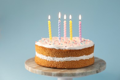 Photo of Tasty cake with colorful candles on light blue background, closeup