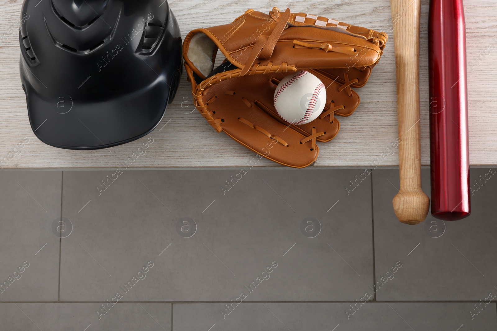 Photo of Baseball bats, batting helmet, leather glove and ball on wooden bench indoors, above view. Space for text