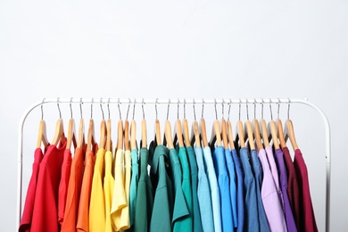 Photo of Rack with bright clothes on light background. Rainbow colors