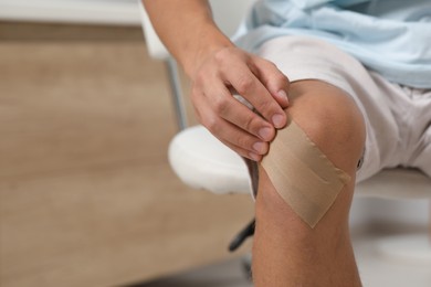 Photo of Man putting sticking plaster onto knee indoors, closeup. Space for text