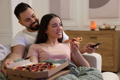 Photo of Happy young couple watching tv and eating pizza on sofa in living room. Space for text