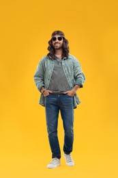 Photo of Stylish hippie man in sunglasses on orange background