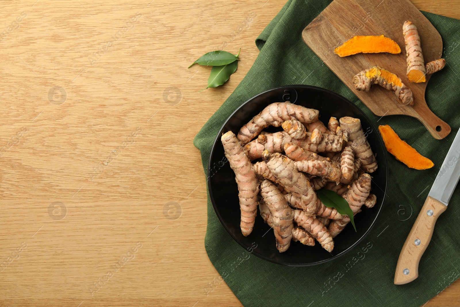 Photo of Many raw turmeric roots and knife on wooden table, flat lay. Space for text