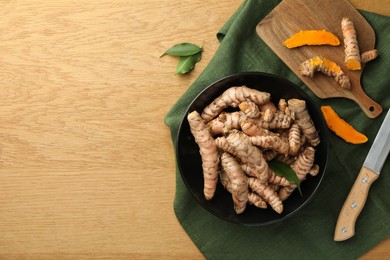 Photo of Many raw turmeric roots and knife on wooden table, flat lay. Space for text