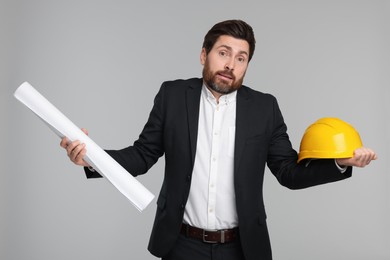 Confused architect with draft and hard hat on gray background