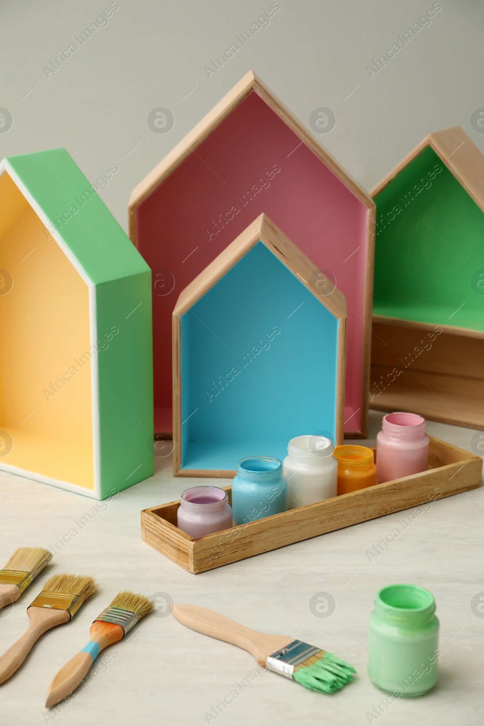 Photo of House shaped shelves, jars of paints and brushes on white table. Interior elements