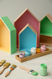 House shaped shelves, jars of paints and brushes on white table. Interior elements