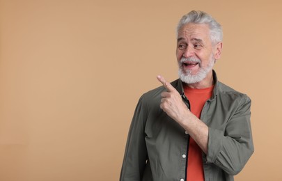 Surprised senior man pointing at something on beige background, space for text