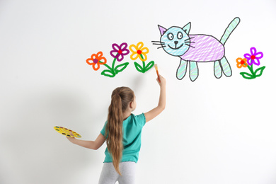 Cute child drawing cat and flowers on white wall indoors