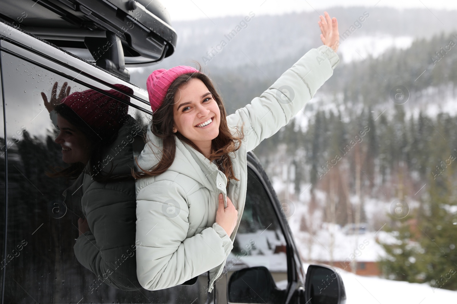 Photo of Happy young woman looking out of car window on road. Winter vacation