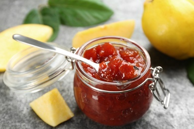 Photo of Delicious quince jam and fruits on grey table