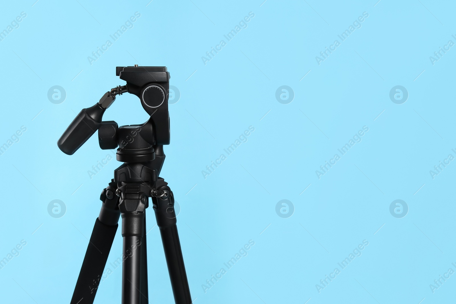 Photo of Modern tripod on light blue background. Space for text
