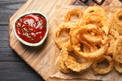 Photo of Homemade crunchy fried onion rings and sauce on wooden background, top view