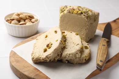 Photo of Tasty halva with pistachios and knife on white table, closeup