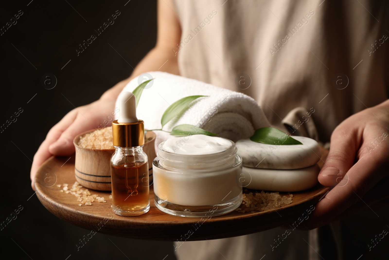 Photo of Woman holding products for spa procedures on dark background, closeup