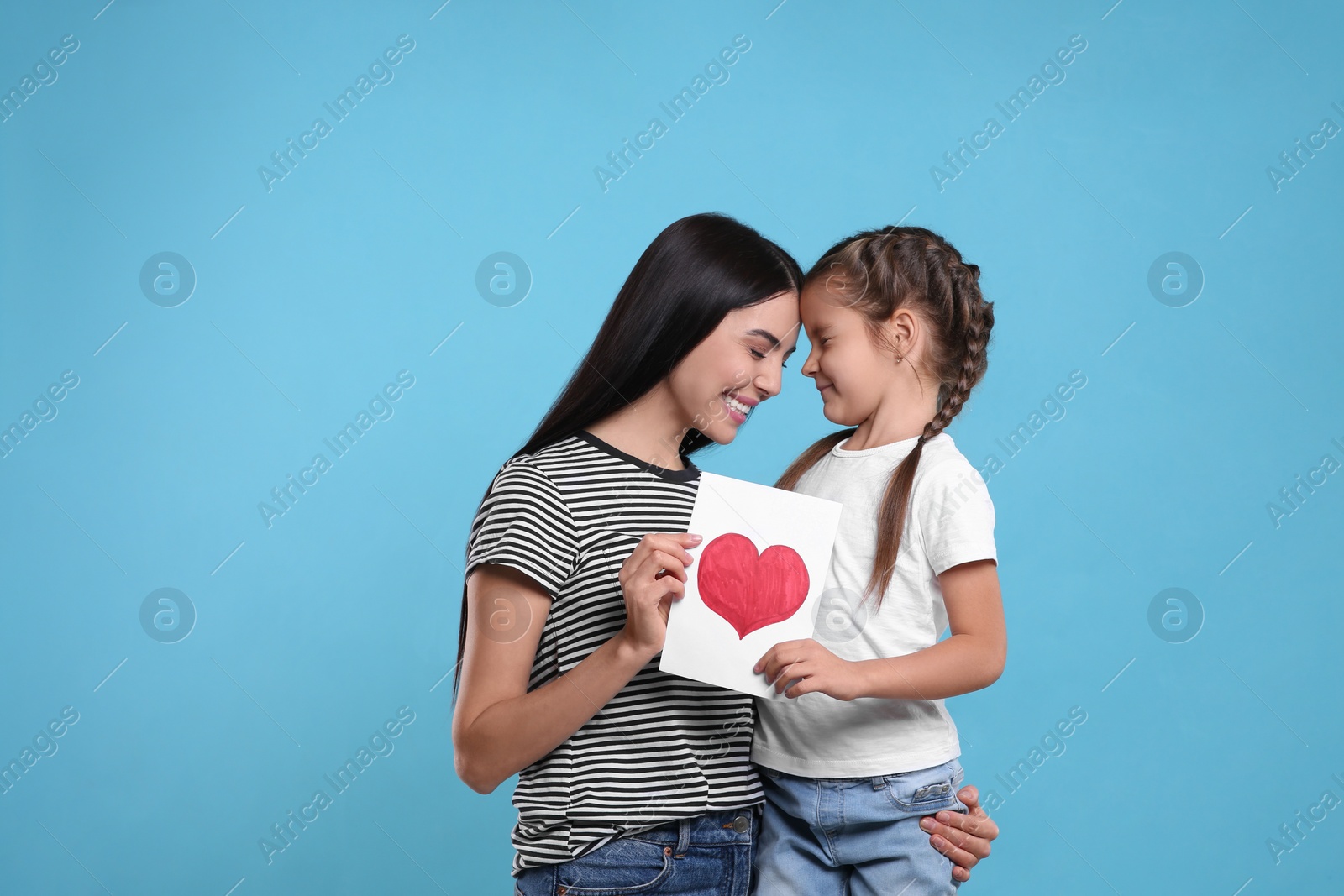 Photo of Happy woman with her cute daughter and handmade greeting card on light blue background. Mother's day celebration