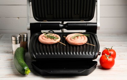 Photo of Electric grill with homemade sausages, rosemary, vegetables and spices on wooden table