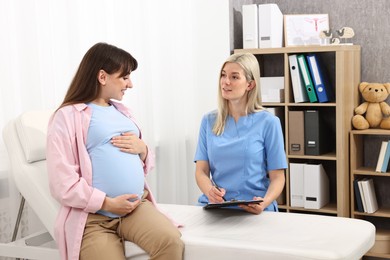 Doctor with clipboard consulting pregnant patient in clinic