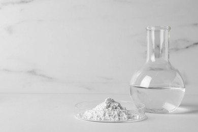 Photo of Petri dish with calcium carbonate powder and laboratory flask on white table. Space for text