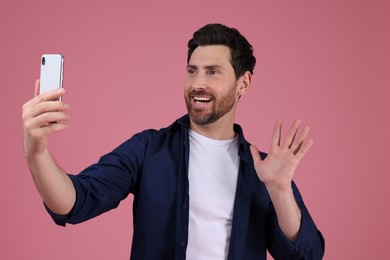 Photo of Smiling man taking selfie with smartphone on pink background