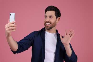 Smiling man taking selfie with smartphone on pink background