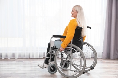 Mature woman sitting in wheelchair near window at home
