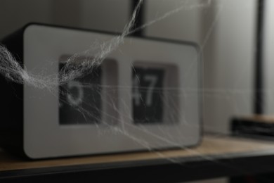 Photo of Cobweb near alarm clock on rack indoors, closeup