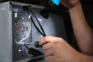 Photo of Repairman with flashlight fixing microwave oven indoors, closeup