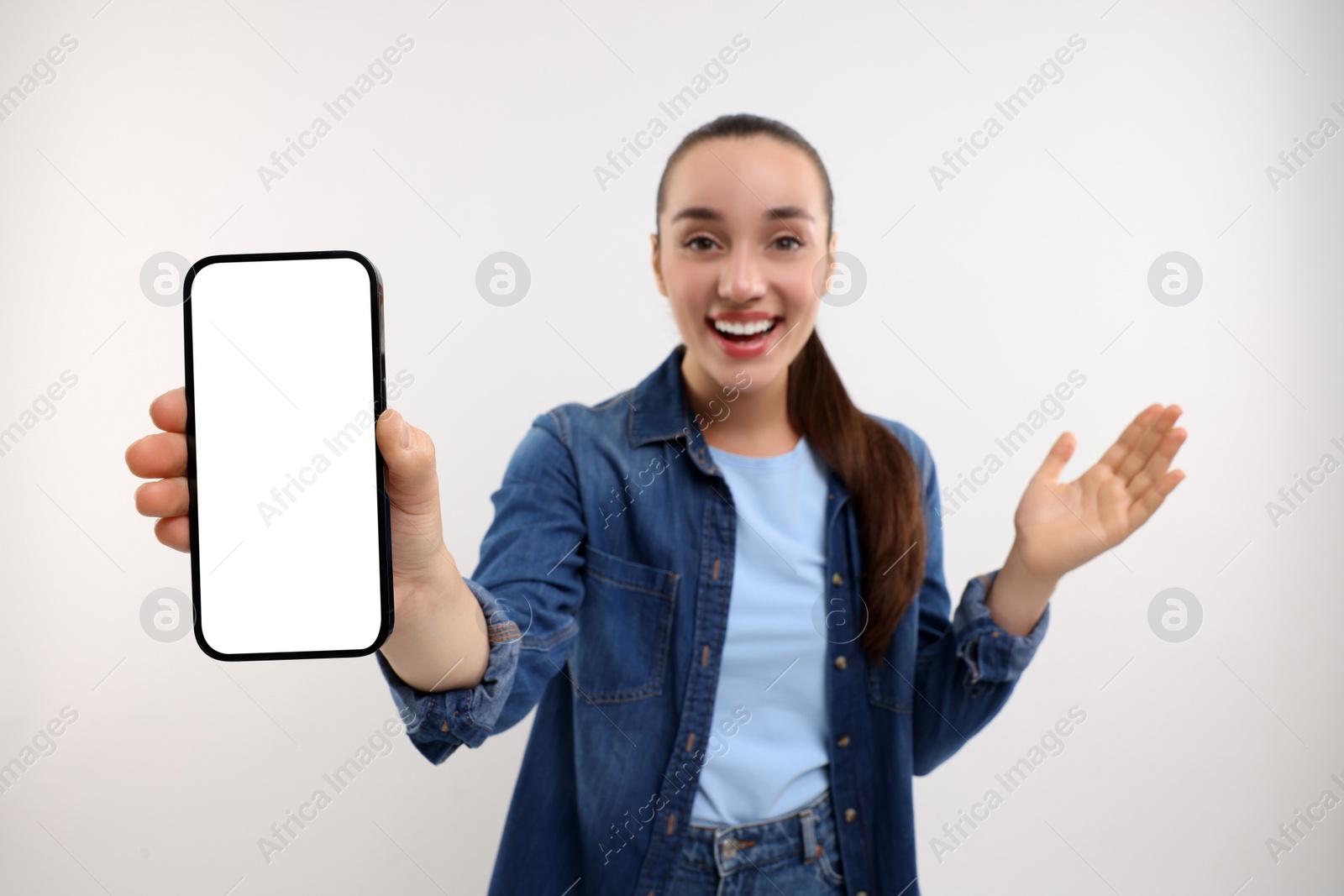 Photo of Surprised young woman showing smartphone in hand on white background, selective focus. Mockup for design