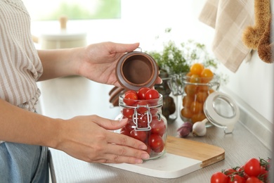 Woman pickling glass jar of tomatoes at counter in kitchen, closeup