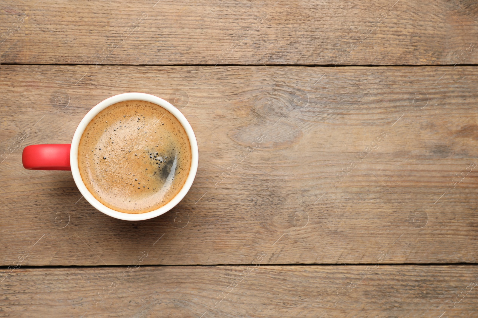 Photo of Aromatic coffee in red cup on wooden background, top view. Space for text