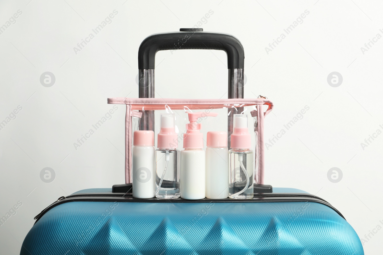 Photo of Cosmetic travel kit in plastic bag on suitcase against light background