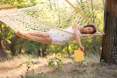 Photo of Young woman with book resting in comfortable hammock at green garden