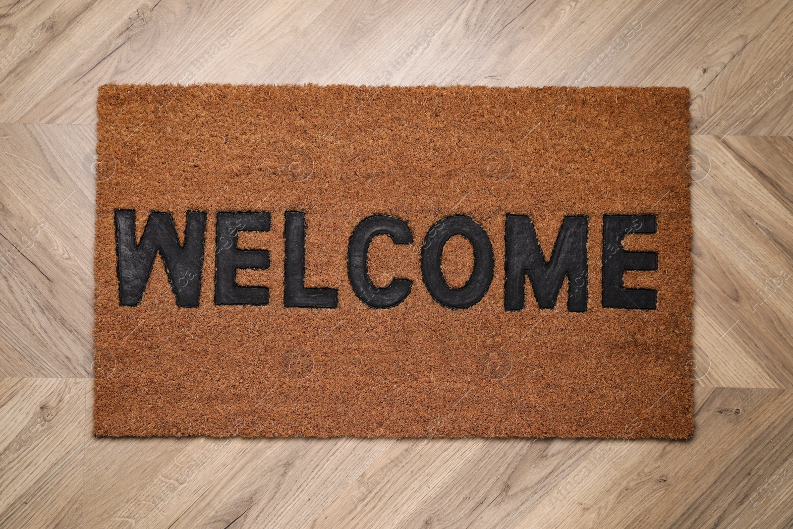 Photo of Stylish door mat with word Welcome on wooden floor, top view