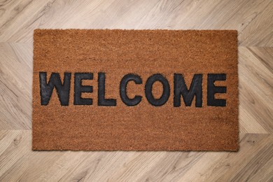 Stylish door mat with word Welcome on wooden floor, top view