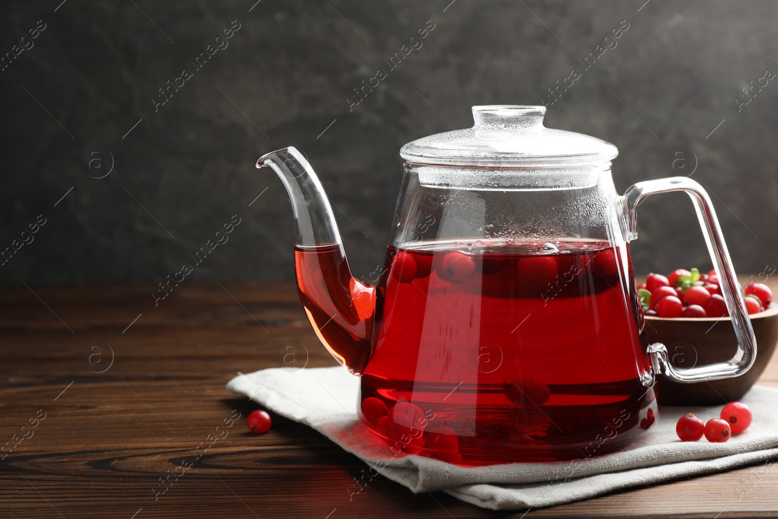 Photo of Tasty hot cranberry tea in teapot and fresh berries on wooden table