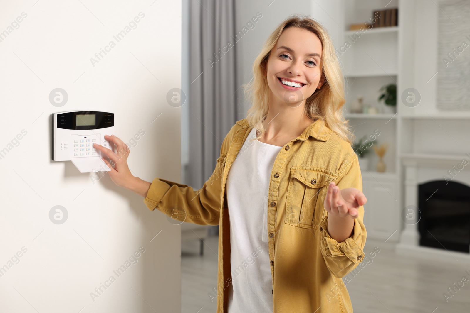 Photo of Smiling woman entering code on home security system in room