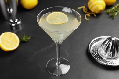 Photo of Martini glass of refreshing cocktail with lemon slice, fresh fruits and hand citrus squeezer on black table