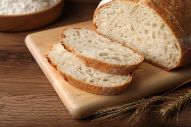 Photo of Cut tasty sodawater bread and wheat spikes on wooden table
