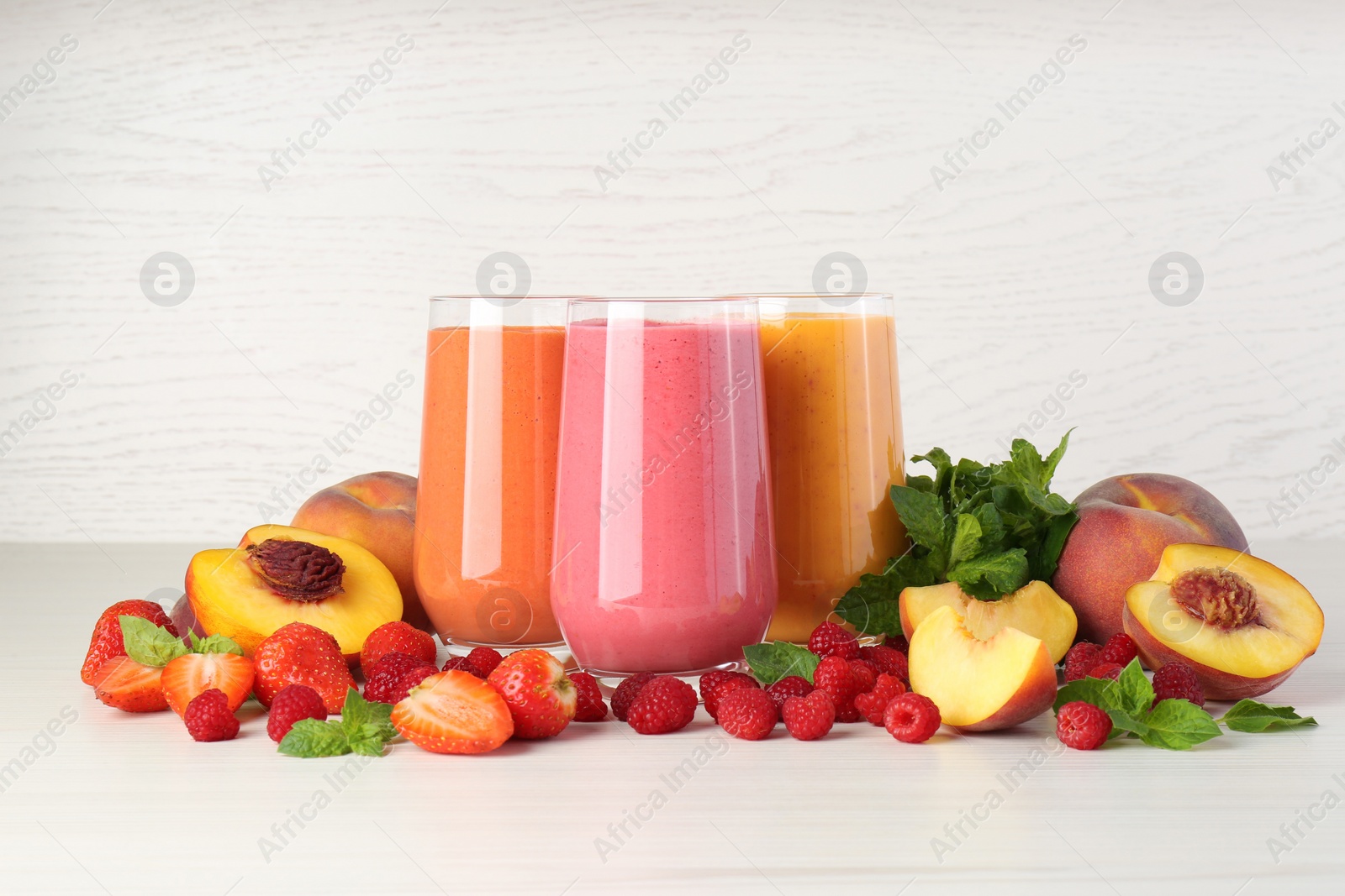Photo of Fresh colorful fruit smoothies and ingredients on white table against wooden wall